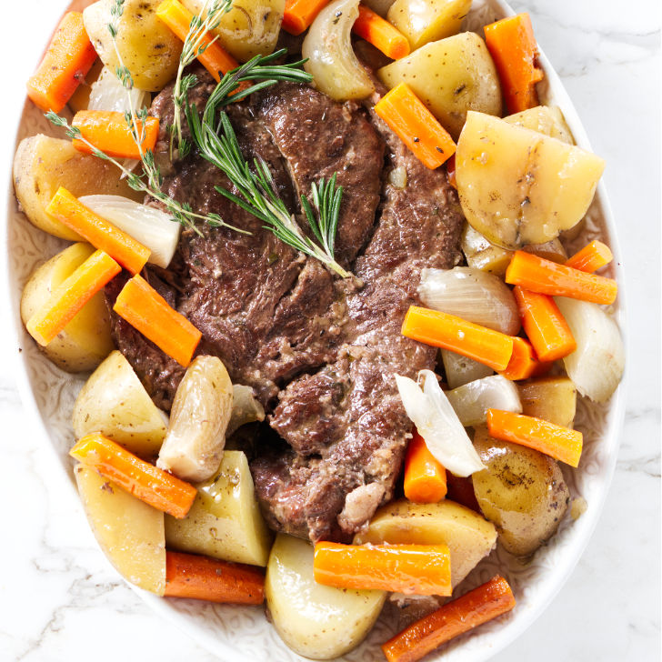 Pot roast in a serving dish with herbs and vegetables.
