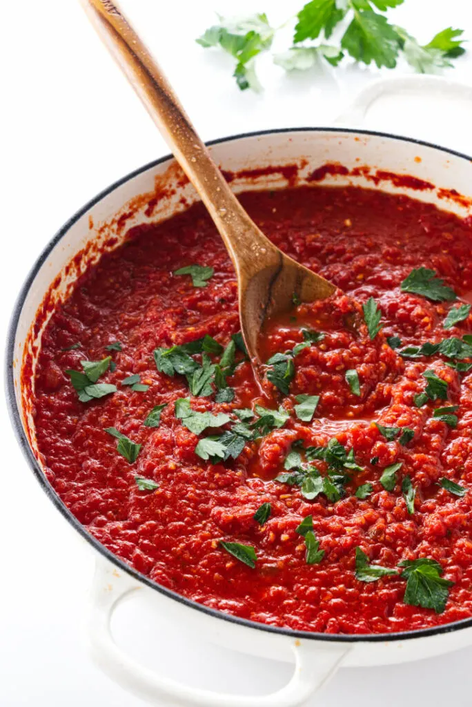 A saucepan of tomato sauce and chopped basil.