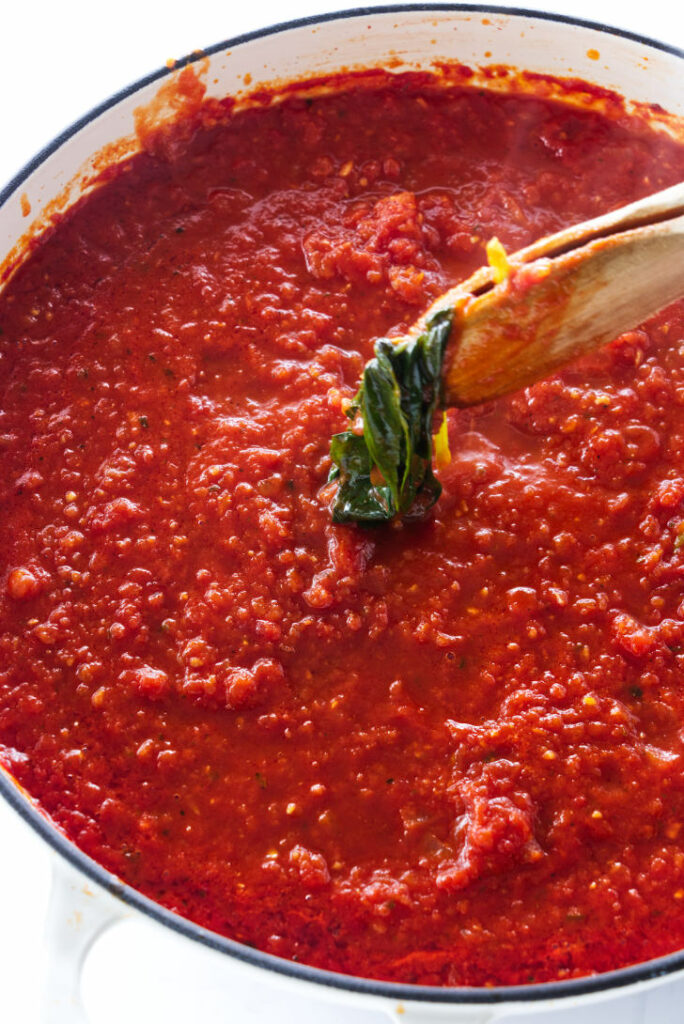 Tongs removing some basil from a pan of tomato sauce.