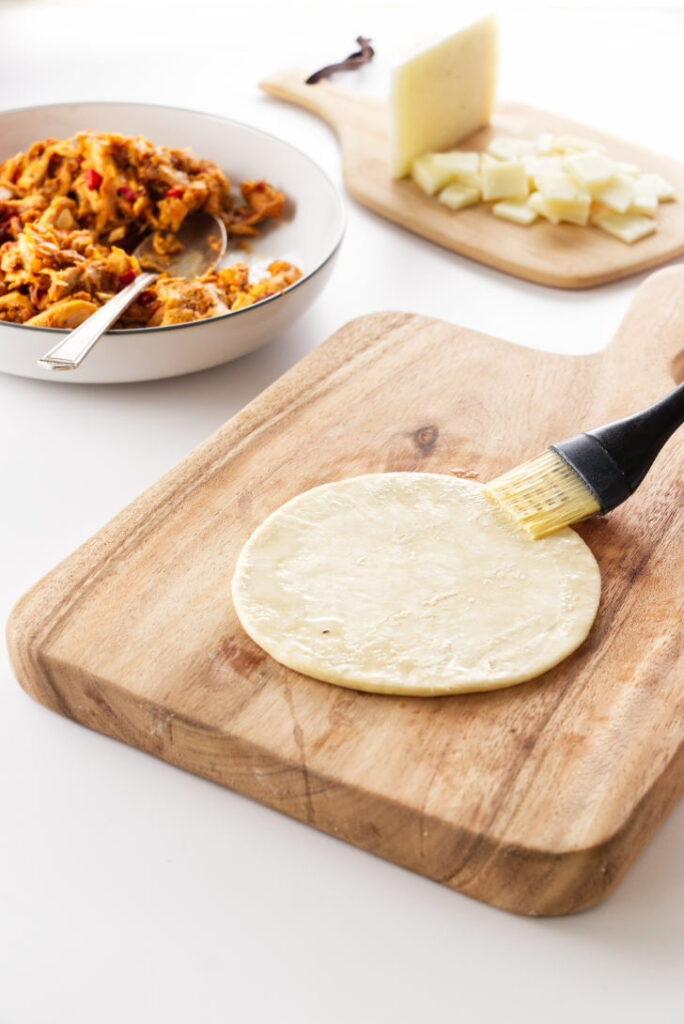 empanada dough with egg wash being brushed on