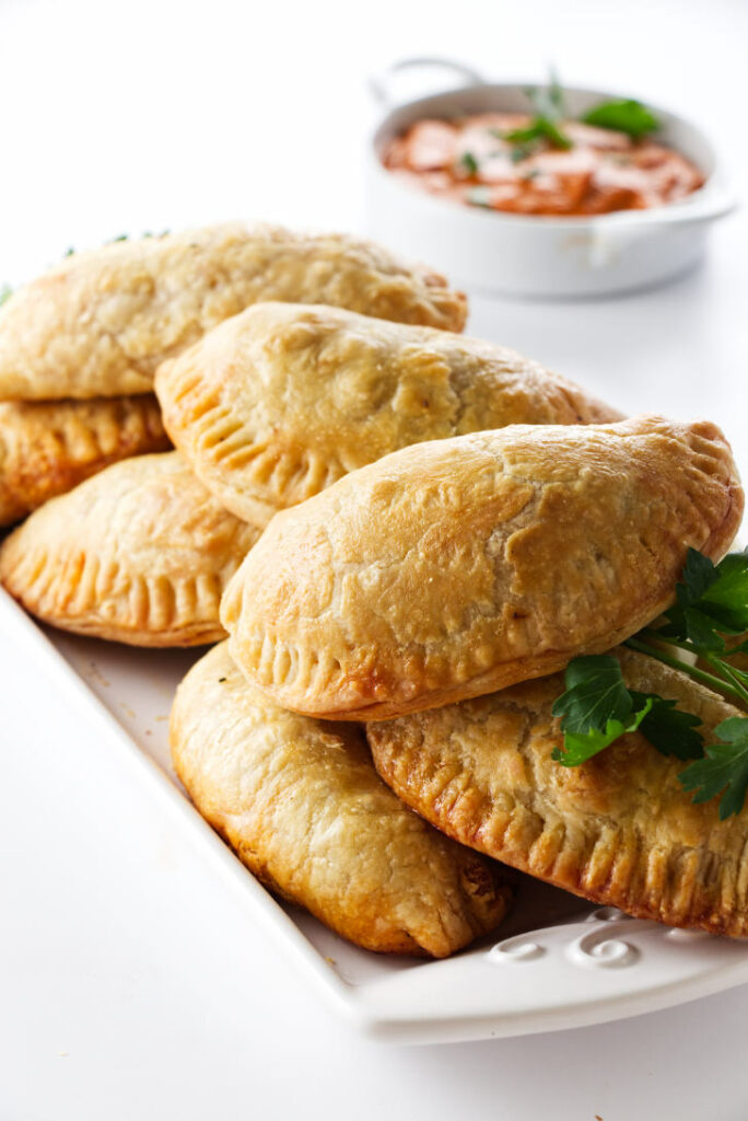 A plate piled with Spanish Chicken empanadas, romesco sauce in background