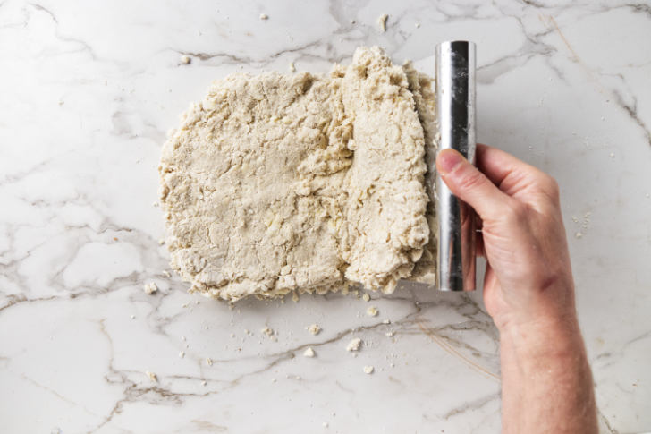 Using a bench scraper to fold biscuit dough.