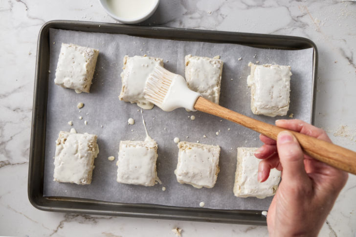 Brushing cream on top of biscuits before baking.