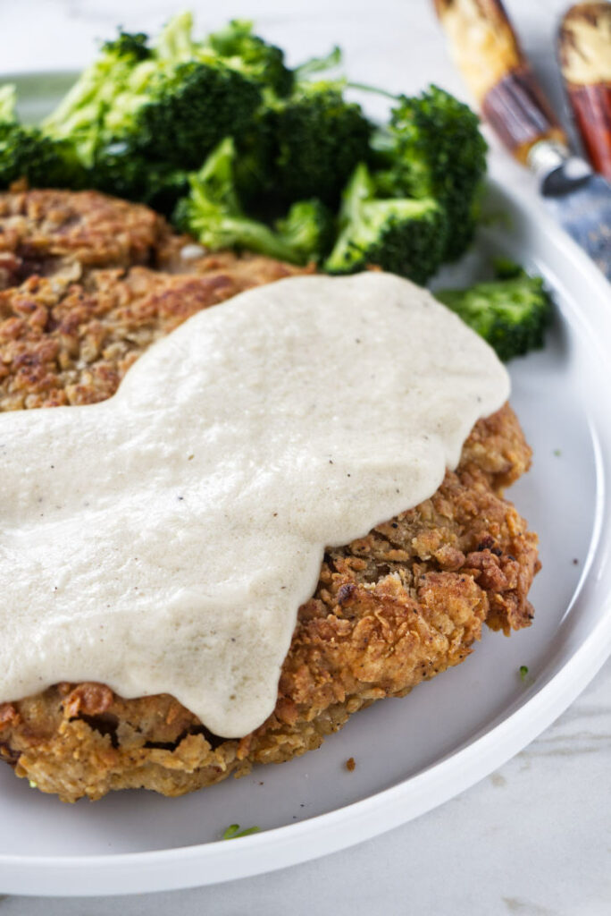A plate with fried venison steak, cream gravy, and broccoli.