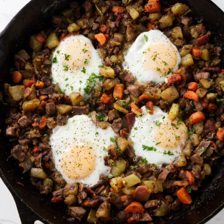 Beef and potato hash in a skillet with eggs on top.