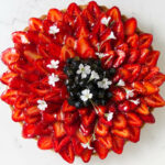 A fruit tart decorated with red strawberries, blueberries, and white flowers.