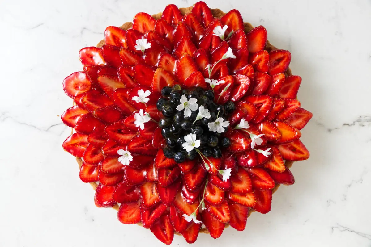 A fruit tart decorated with red strawberries, blueberries, and white flowers.
