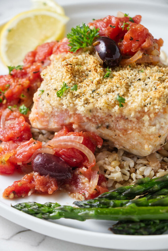 A fillet of halibut on a bed of rice with chunky tomato sauce.