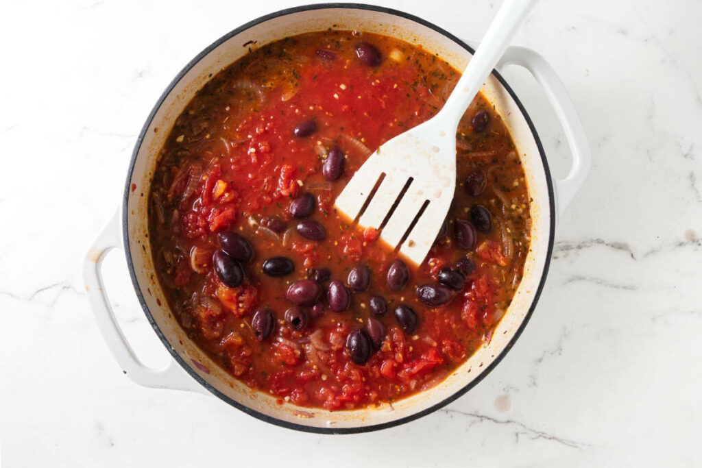 Adding Kalamata olives to tomato sauce.