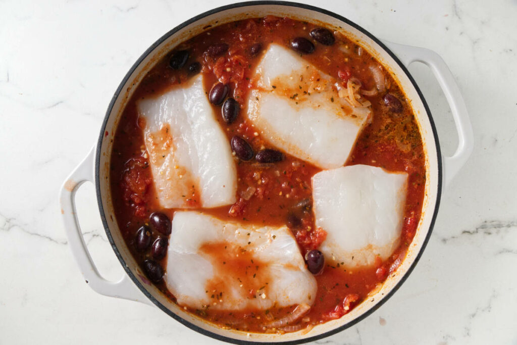 Adding halibut to a skillet filled with tomato sauce.