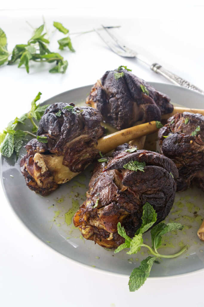 Braised Persian lamb shanks on a plate with mint sprigs
