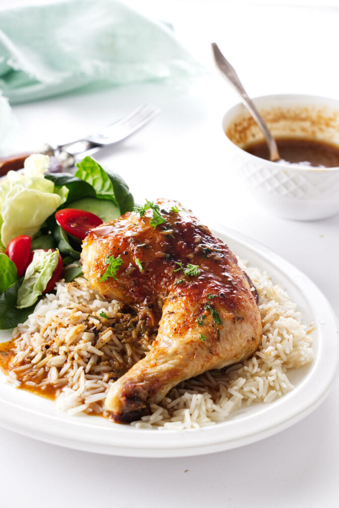 Baked chicken quarters on a plate with rice and sauce.