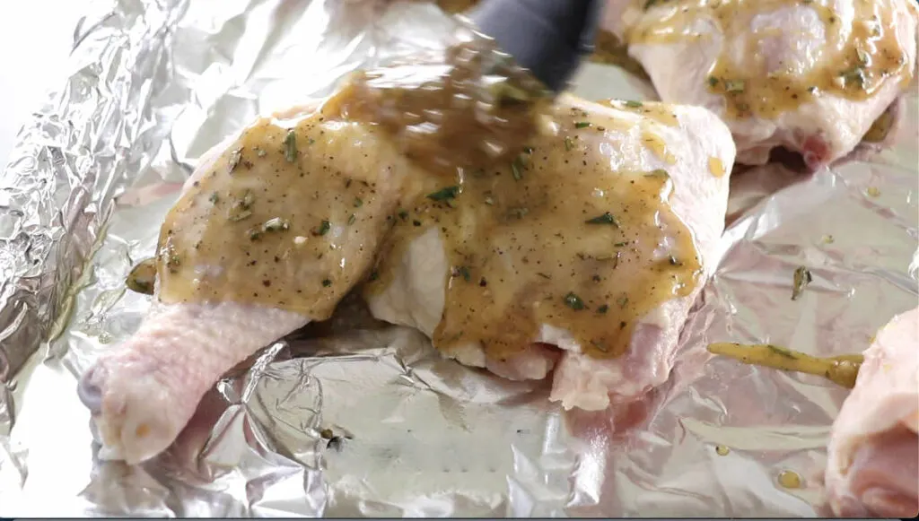 Brushing sauce over the top of a chicken quarter.