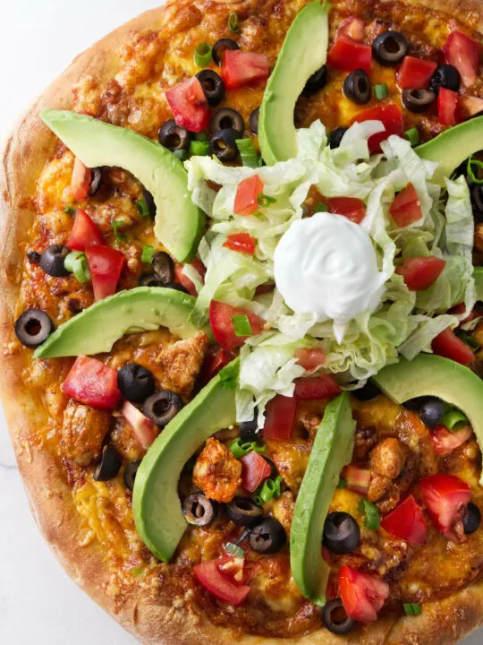 A pizza topped with chicken and taco fixings.