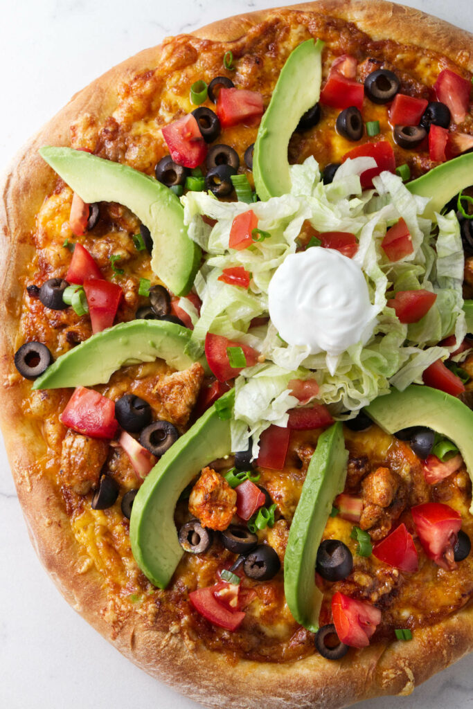 A pizza topped with chicken and taco fixings.