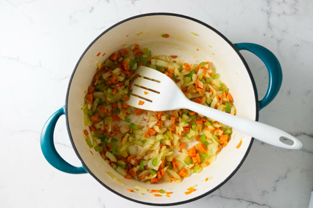 Sauteeing carrots, onions, and celery in a pot.