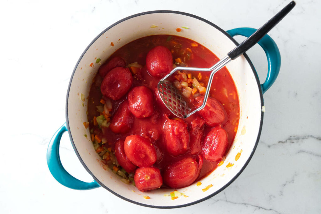 Smashing whole tomatoes in a soup pot.