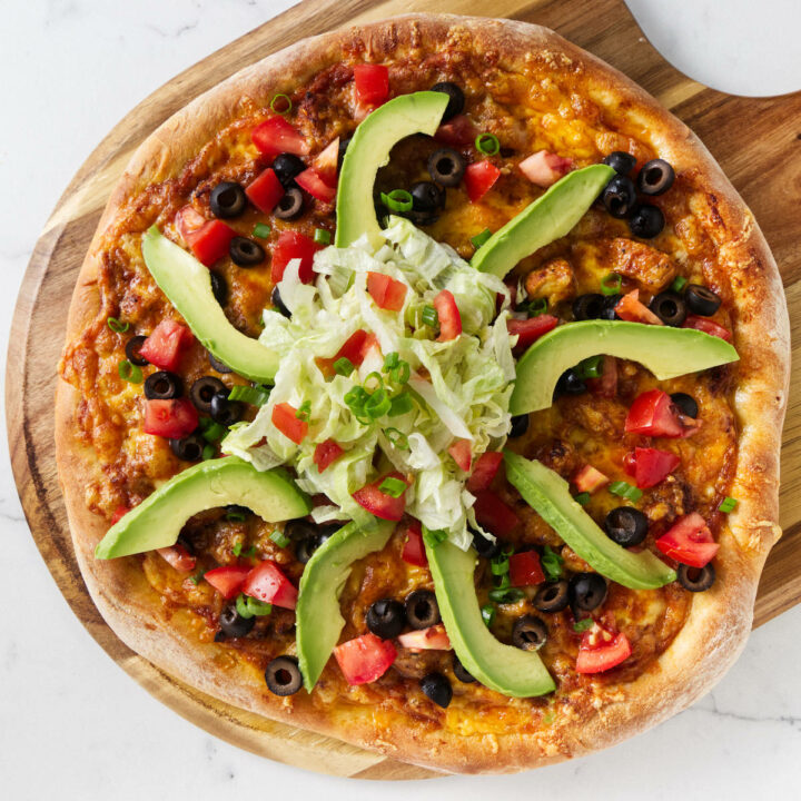 A chicken taco pizza garnished with taco fixings.