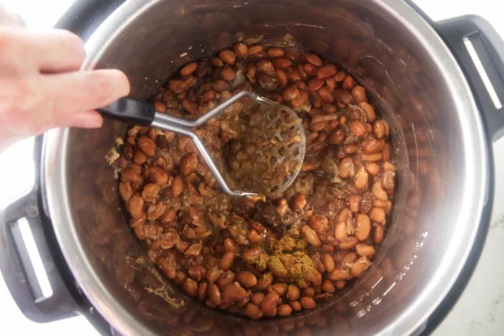 Mashing beans with a potato masher.