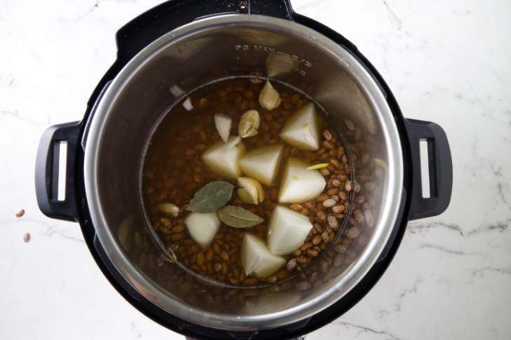 Dried pinto beans in an Instant Pot with broth, onions, and garlic.