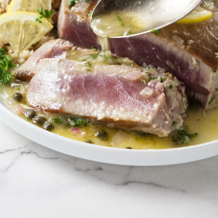 Drizzling piccata sauce over tuna steaks.