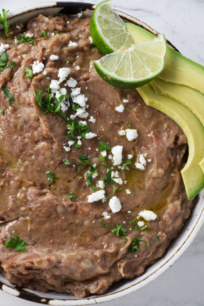 Refried beans topped with cheese, parsley, guacamole, and lime.