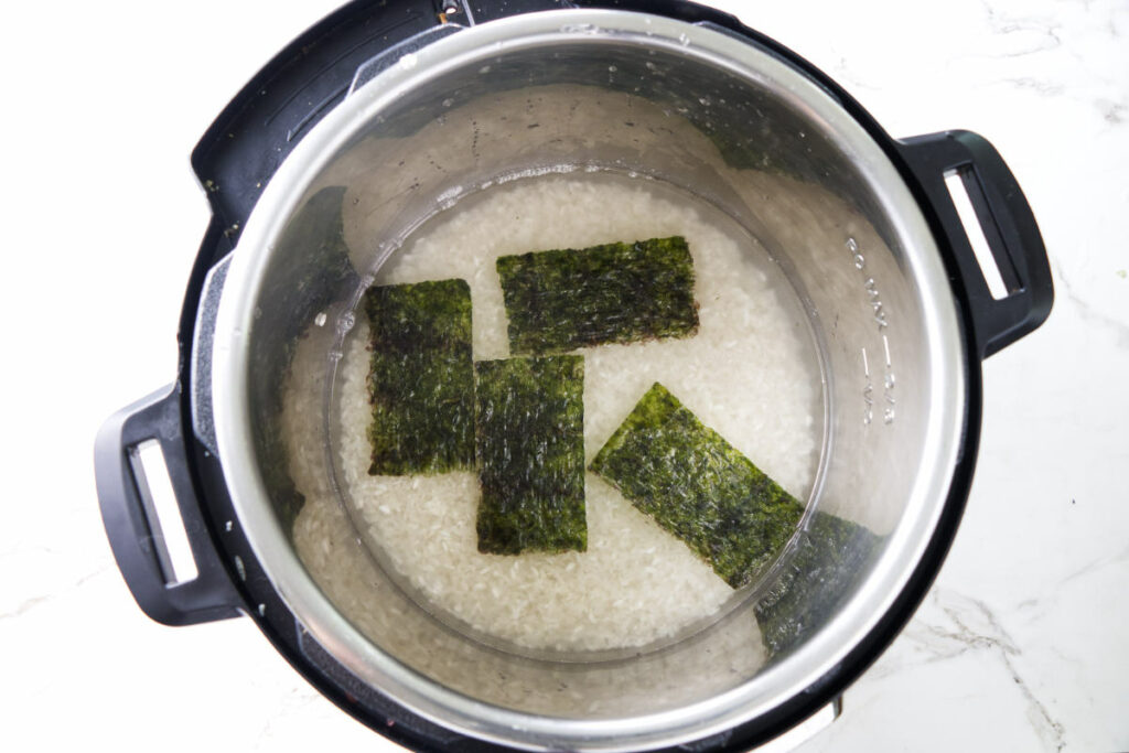 Adding dried seaweed to an Instant Pot filled with sushi rice and water.