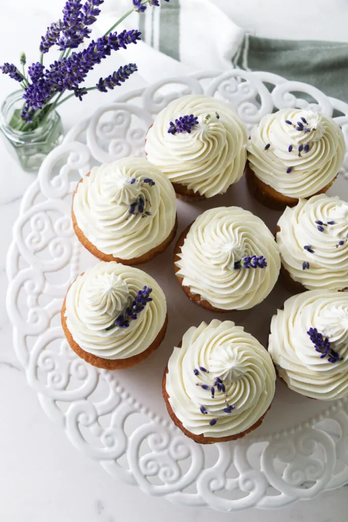 Overhead view of Ermine frosted lavender cupcakes. lavender flowers and towel in background