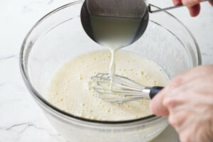 Adding hot milk to the lemon and egg mixture to temper the eggs.