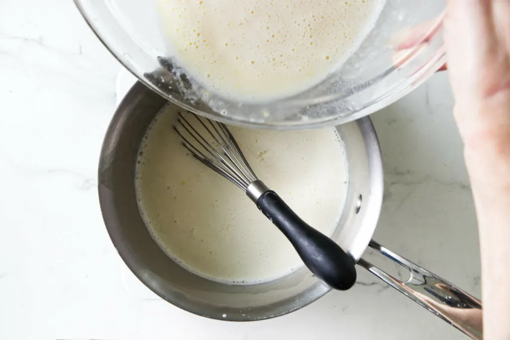 Pouring tempered eggs into a hot milk mixture.