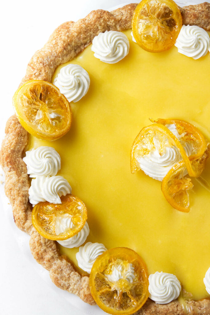 A Lemon custard pie topped with dollops of whipped cream and candied lemon.
