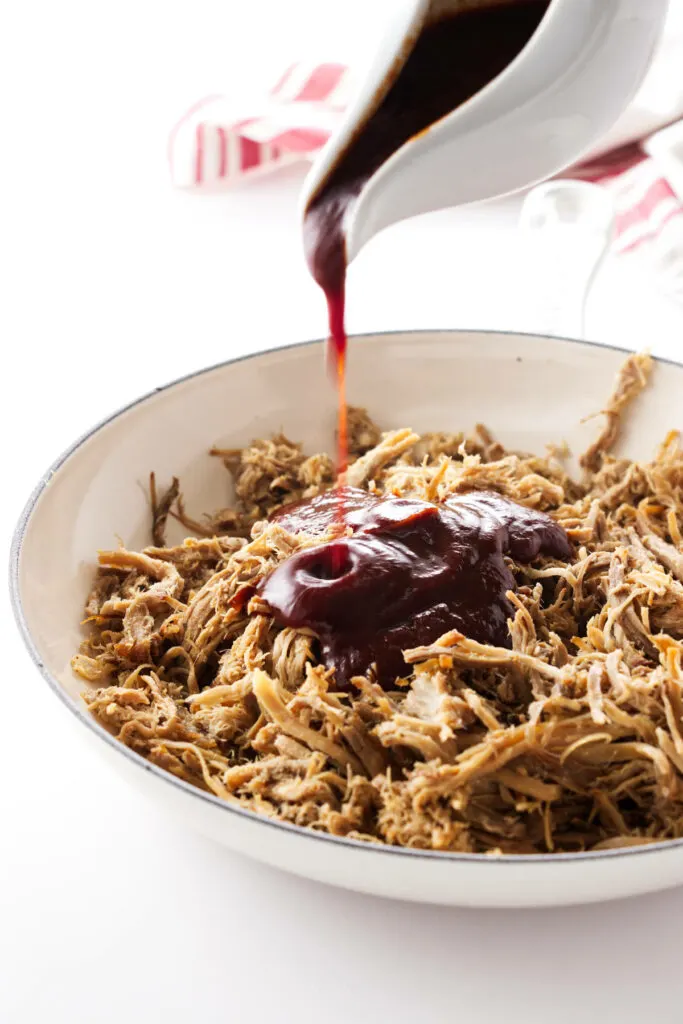 Pulled pork in a dish with a pour of BBQ sauce