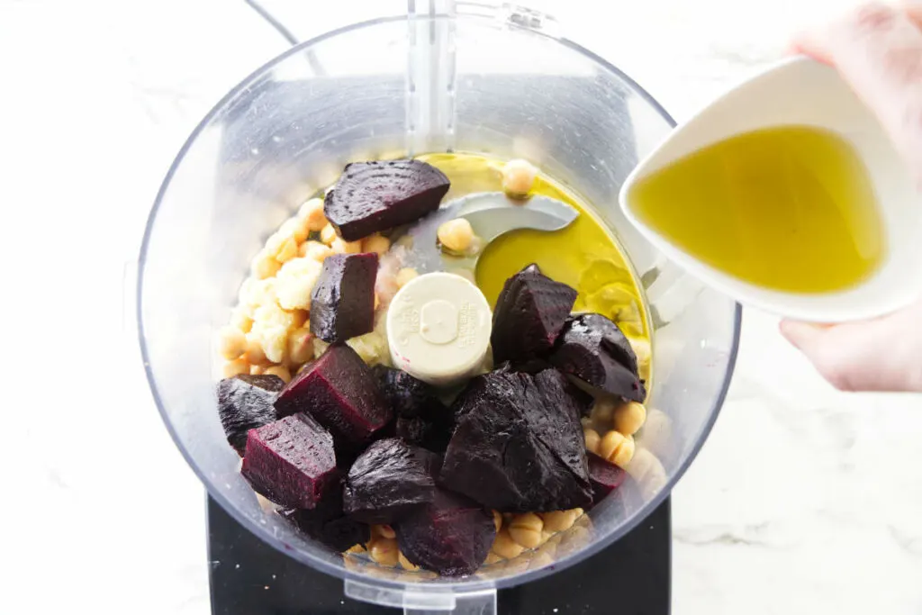 Adding beets, beans, and olive oil to a food processor.