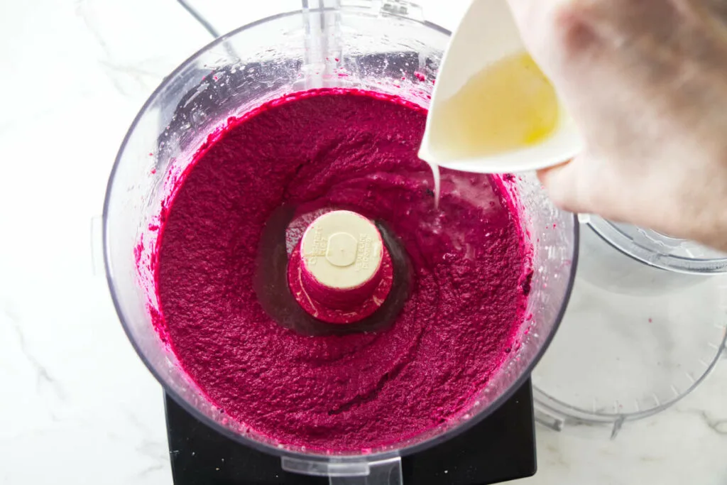 Adding liquid to beet hummus.