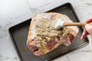 Slathering mustard on a pork shoulder.