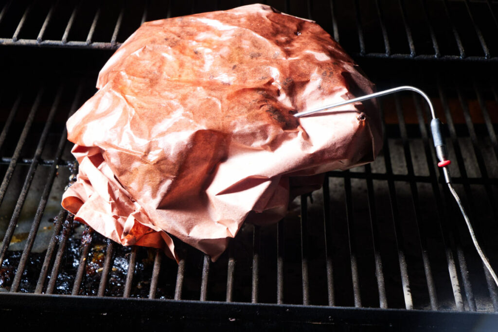 A pork shoulder wrapped in butchers paper on the grill.