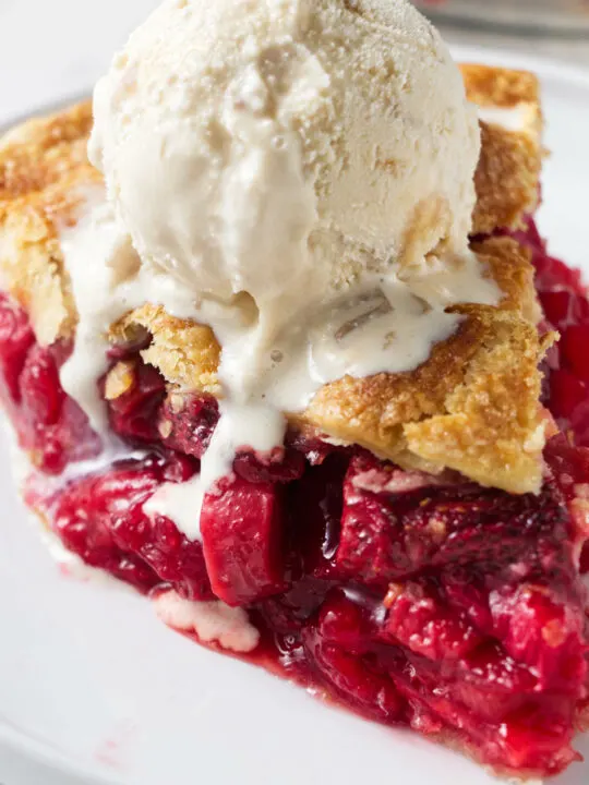 A slice of strawberry rhubarb pie topped with vanilla ice cream.