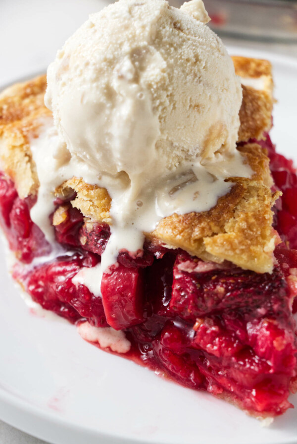 A slice of strawberry rhubarb pie topped with vanilla ice cream.