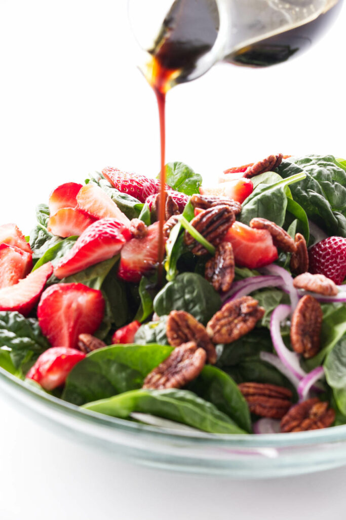 Dressing being pored on a bowl of strawberry spinach salad