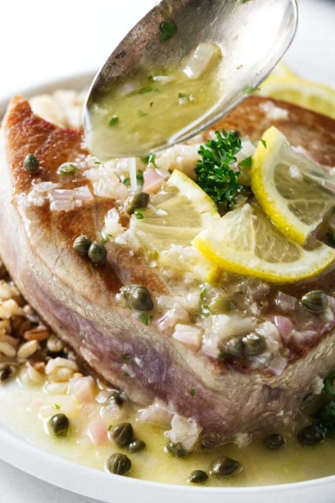 Drizzling lemon caper sauce over a tuna steak.