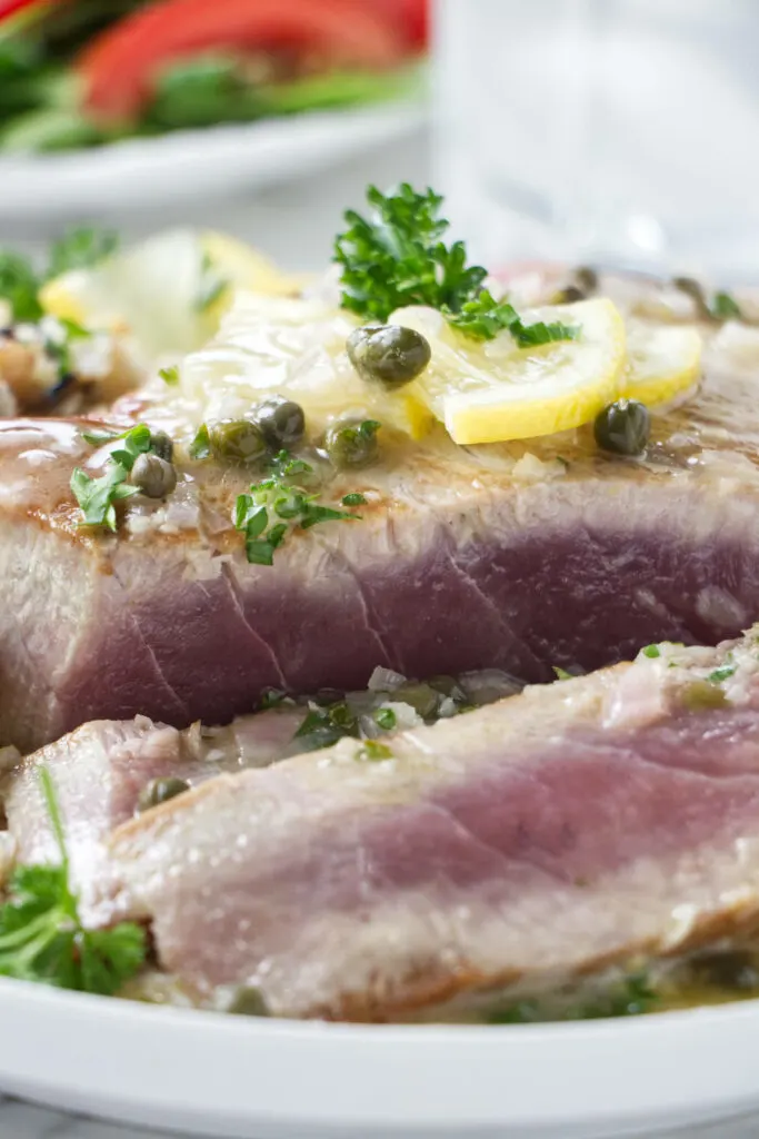 A tuna steak topped with lemon slices and piccata sauce.