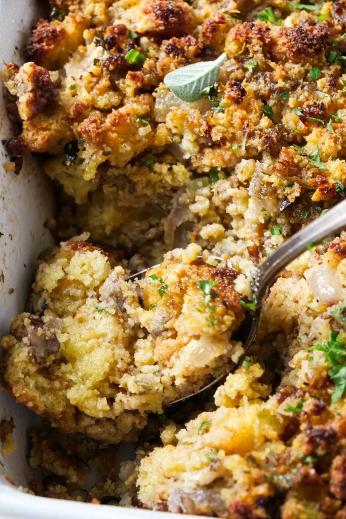 A spoon scooping stuffing out of a casserole dish.