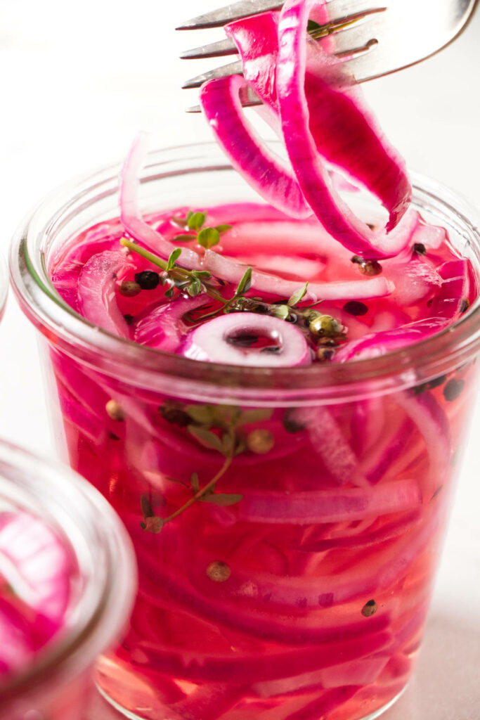 A fork scooping out some pickled onions from a jar.