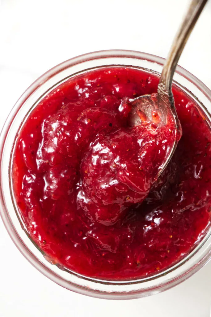 A spoon scooping up some jam from a jar.