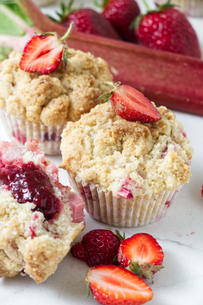 Muffins on a counter with fresh strawberries and rhubarb.