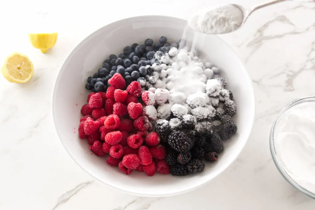 Sugar mixture being added to a dish of mixed berries.
