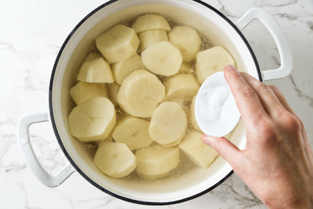 Adding salt to a pot of potatoes and water.
