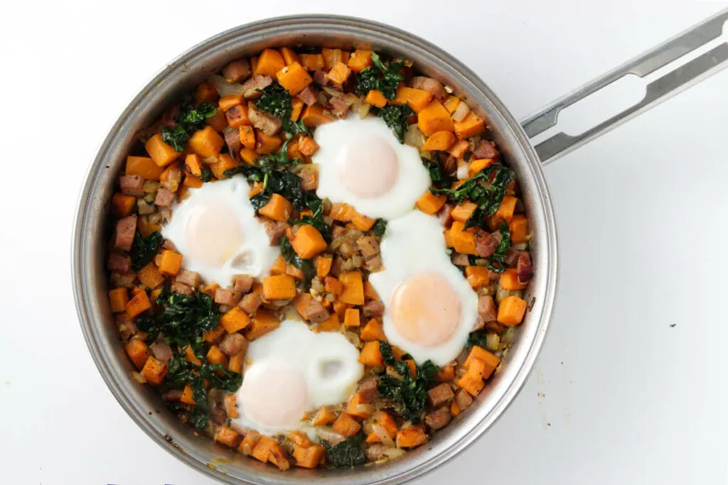 Steamed eggs on top of sweet potato hash in a skillet.