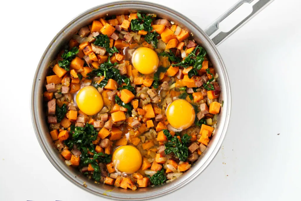 Raw eggs on top of breakfast sweet potatoes in a skillet.