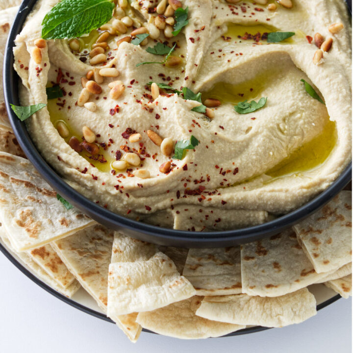A bowl of hummus garnished with pine nuts and olive oil.